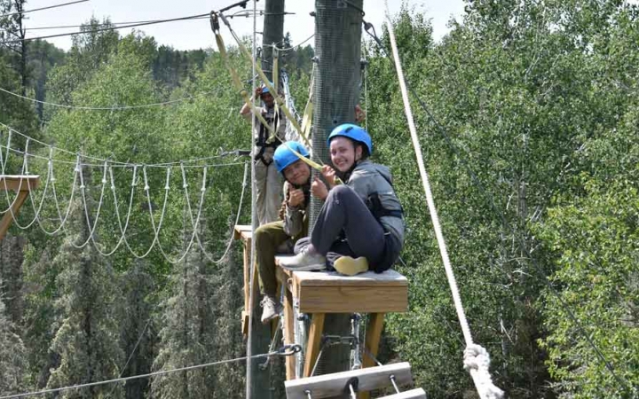 two outward bound students sit atop a platform during a ropes course exercise with outward bound